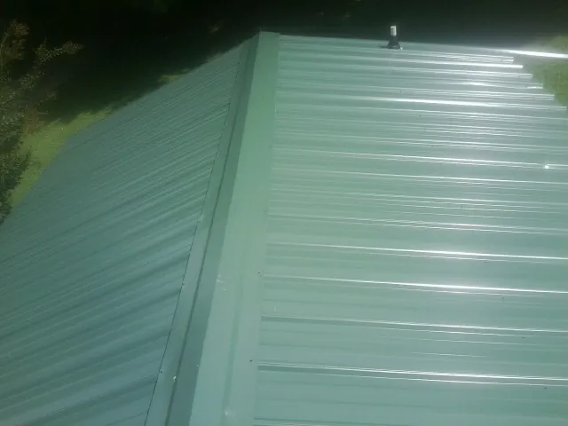 New green metal panels meeting at the ridge of a roof — Flat Roof Repair work by our crew in Duncannon