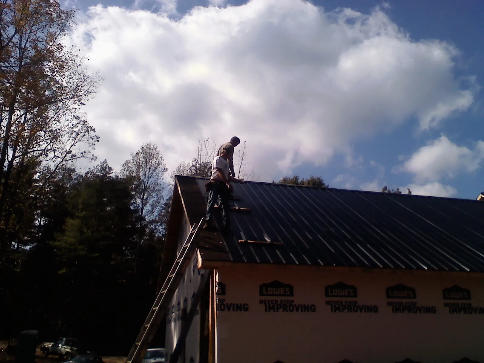 Roofer fastening dark metal panels high against a cloudy sky, from a Roof Inspection job in Duncannon