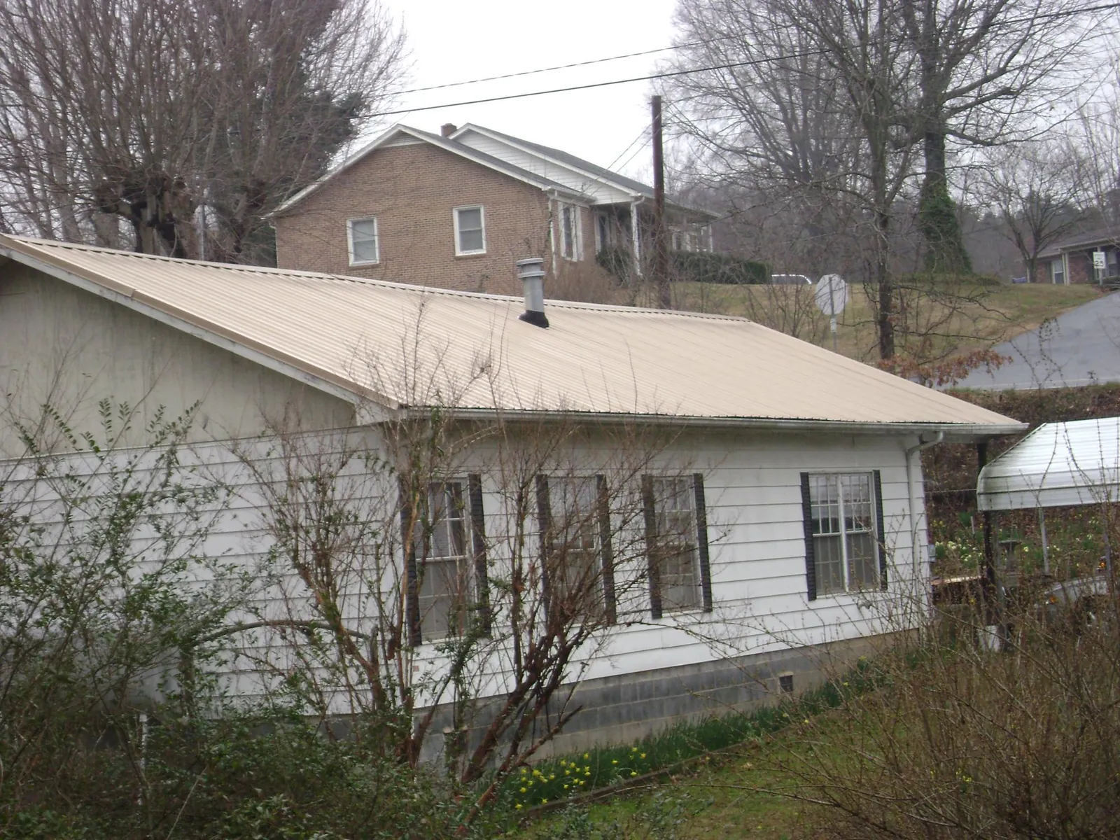 Tan metal roof on a white sided house set into a hillside — Commercial Roofing by Roofing Brothers in Duncannon